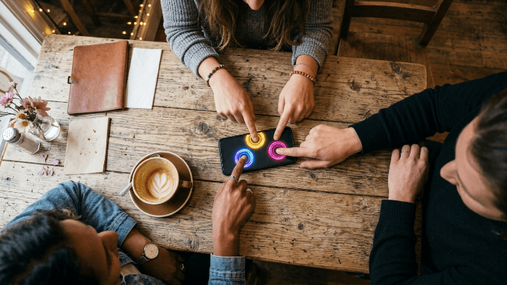 Multiple hands touching a smartphone screen simultaneously to pick a random person using a finger chooser app.